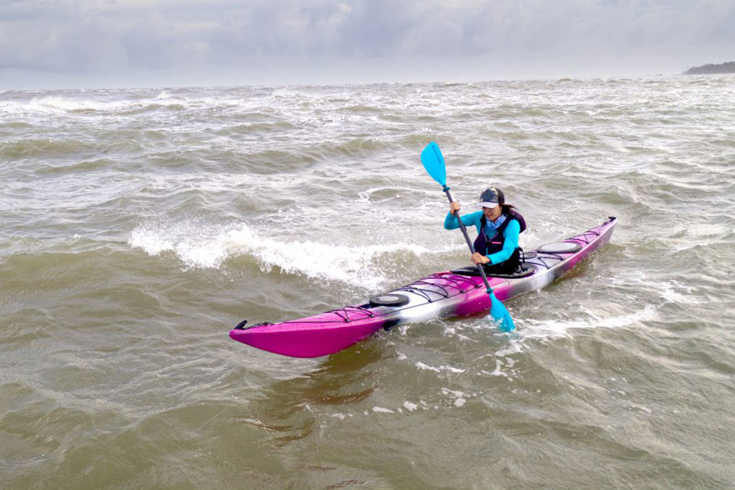 woman paddles kayak in choppy water