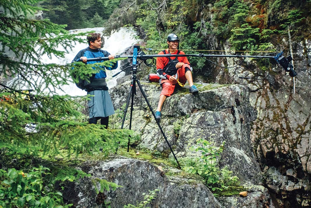 paddling filmmaker uses a boom to film a whitewater kayaker sitting on a rock in front of the raging river