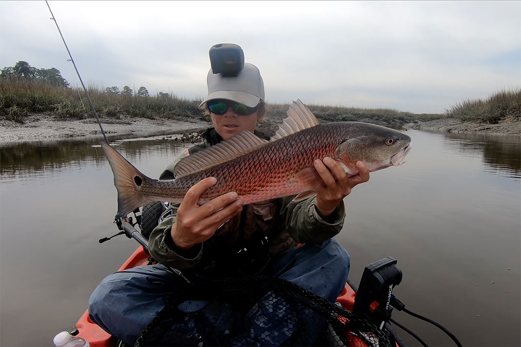 kayak angler holds up redfish before dolphins interrupt his fishing
