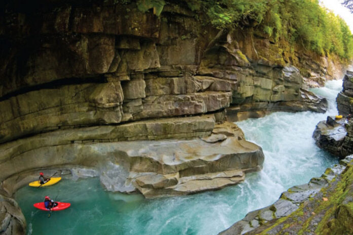 two whitewater kayaks float in the Ashlu River in British Columbia while a third sits on a rocky ledge
