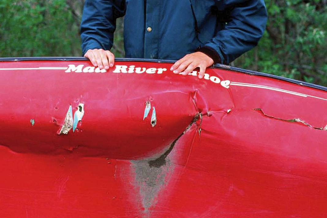 person holds up a damaged canoe with hull in need of repair