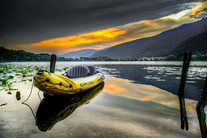 Intex inflatable kayak sits on glassy water in front of a mountain under dramatic clouds