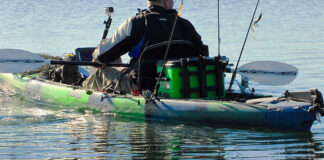 Person padding a green and black sit-on-top fishing kayak with rods