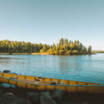 Best Wenonah Canoes For 2026 Wenonah canoe sitting on a lakeshore