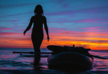 How To Pick The Perfect Women’s Paddleboard woman stands beside paddleboard silhouetted in the sunset