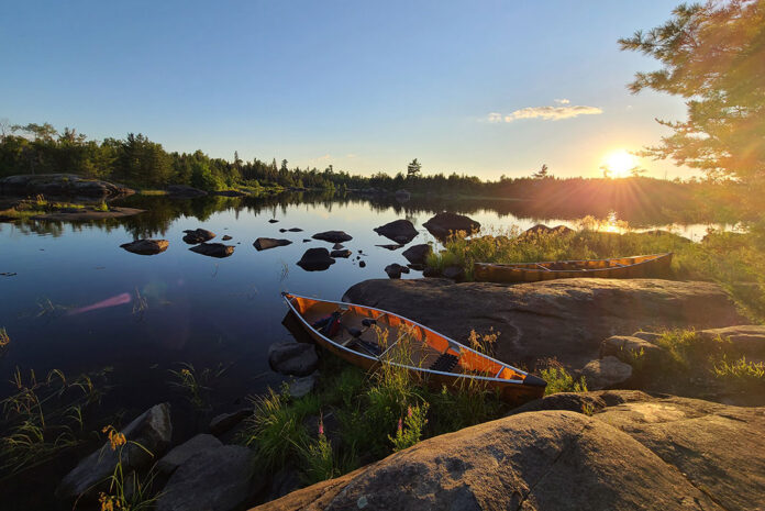 A canoe rests a the edge of a rocky lake in the Boundary Waters at sunrise