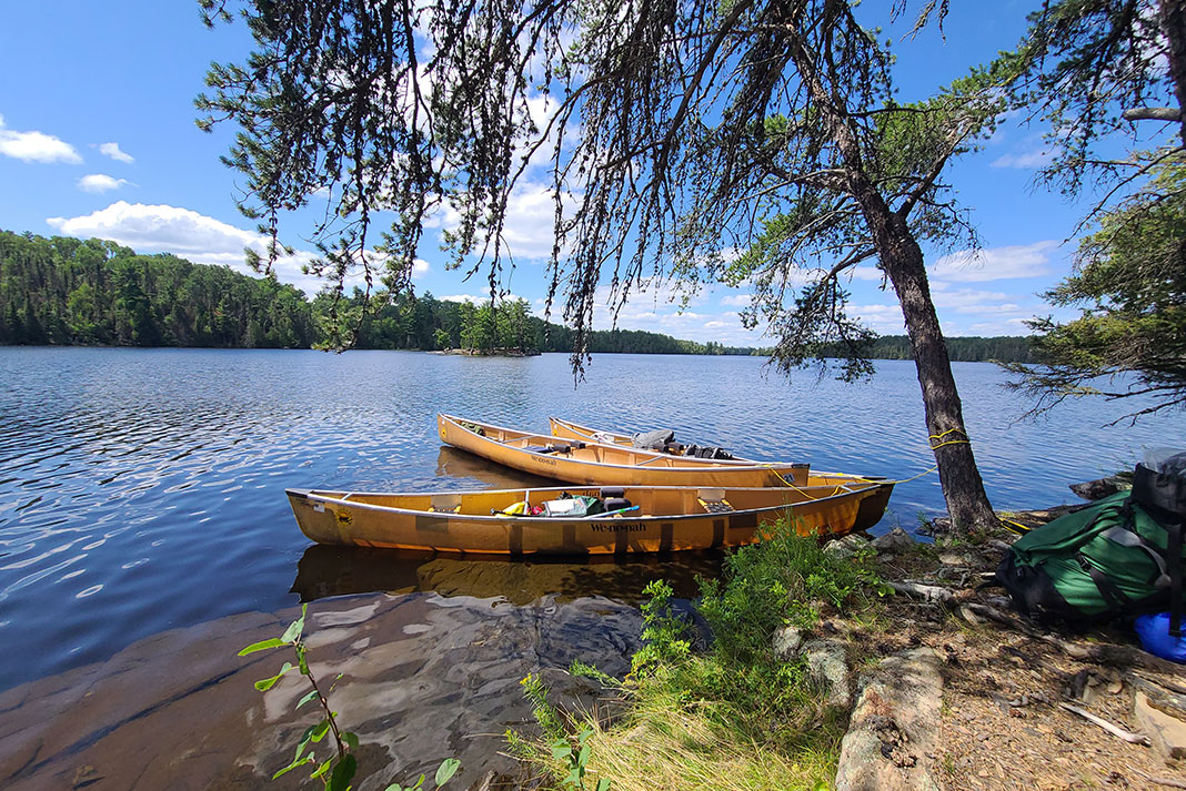 Wenonah canoes sit in the water beside a campsite in the Boundary Waters