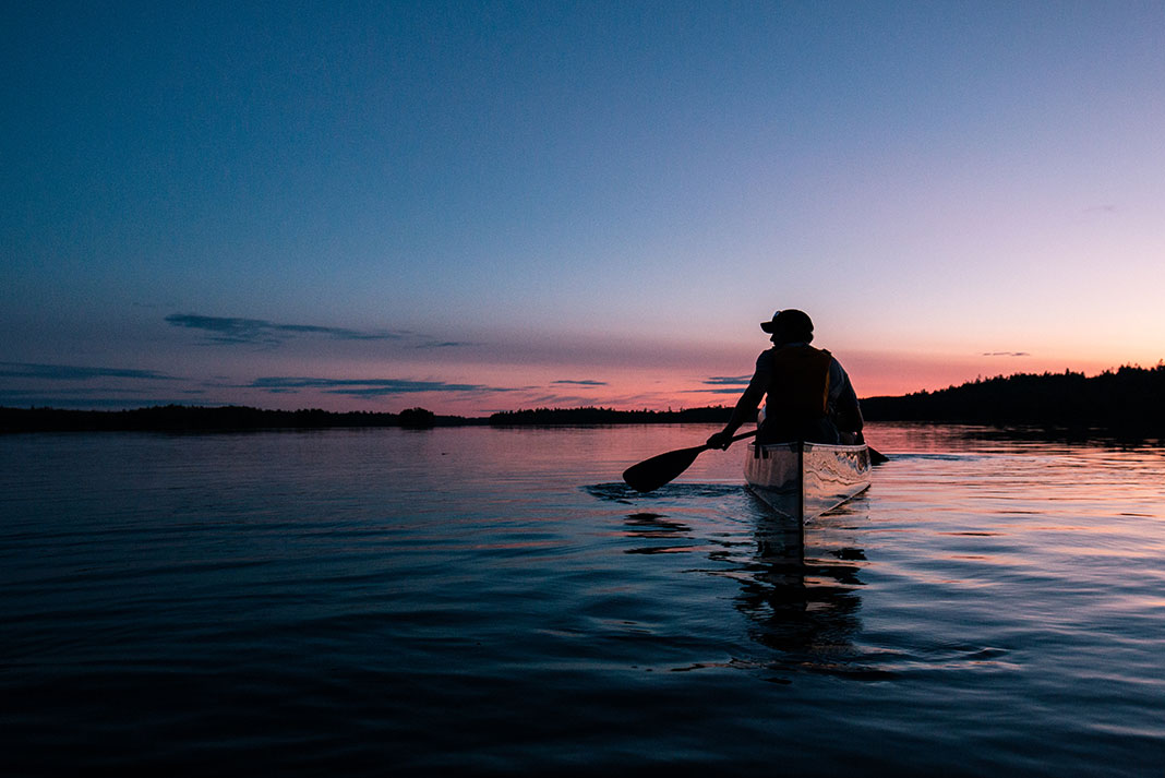 man paddling a canoe in the dusk