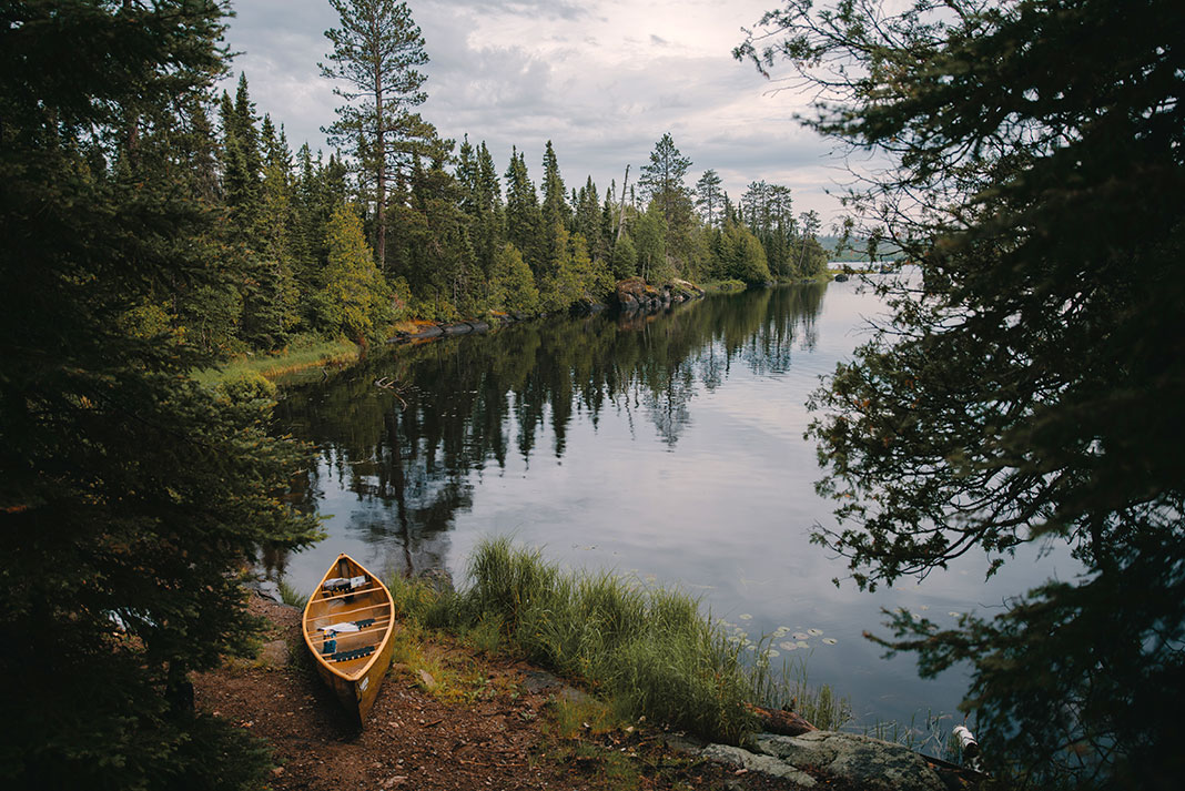 canoe sits beside calm treed lake on cloudy day in Boundary Waters