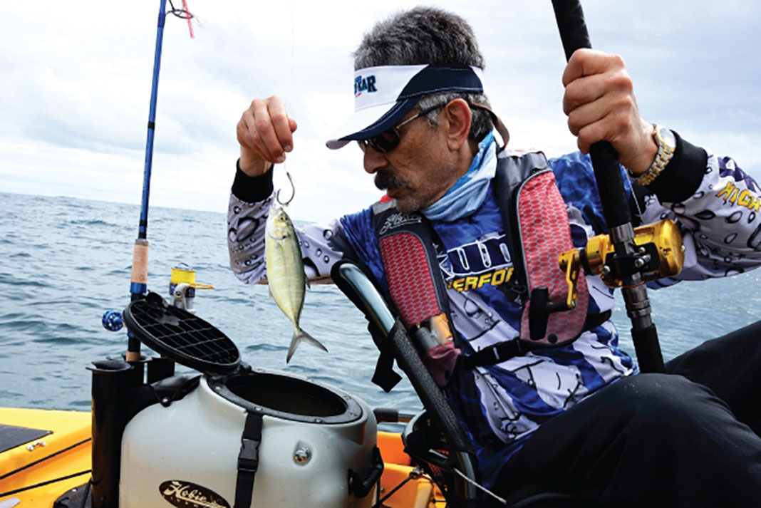 angler puts a live bait fish into his kayak livewell