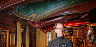 Ken Kelly poses in front of several of his antique courting canoes