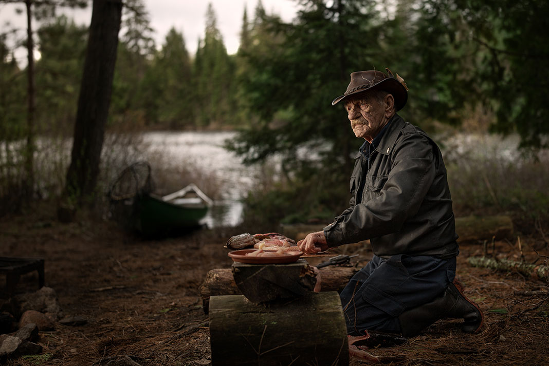 Algonquin fishing guide Frank Kuiack kneels and cleans fish at a campsite with canoe in background