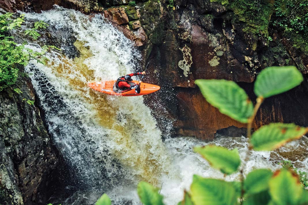 person in whitewater kayak goes off a waterfall with leaves in foreground