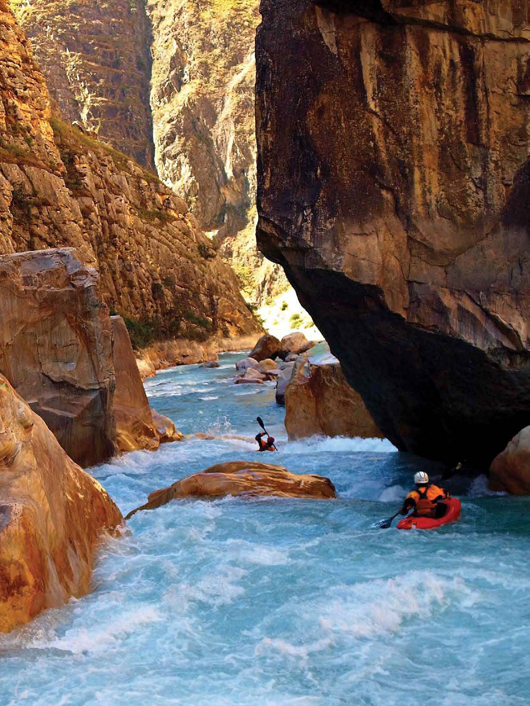 two whitewater kayakers paddle through a rocky, monsoon-flooded canyon in Nepal's Himalaya Mountains