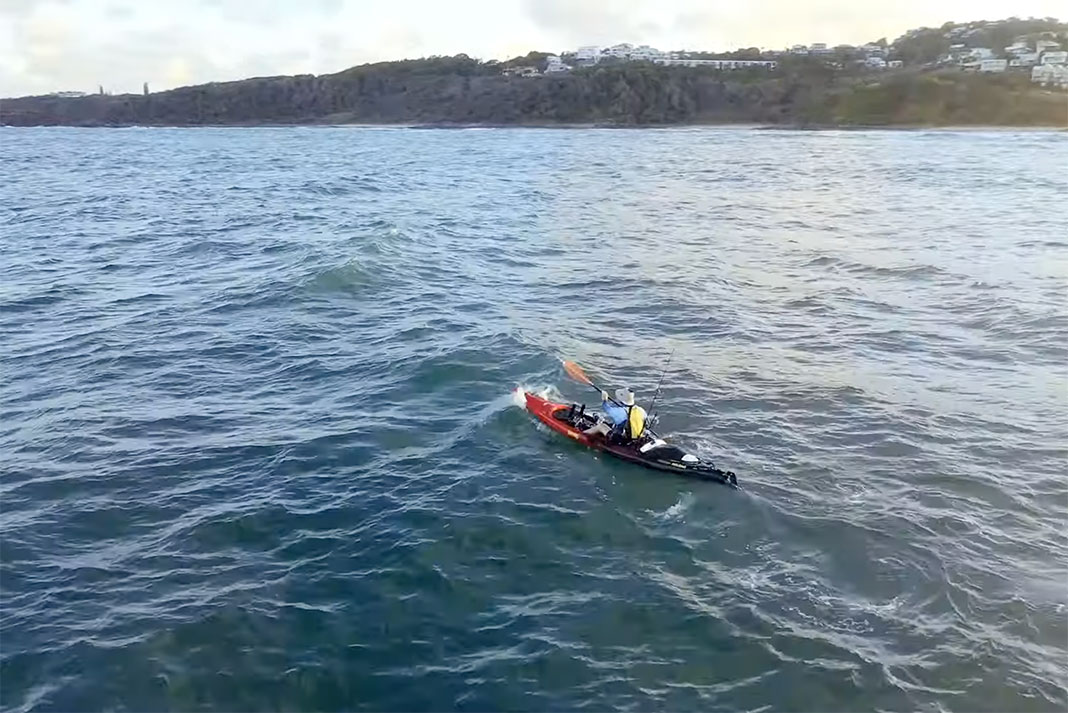 person paddles a kayak out into saltwater with shore in the background
