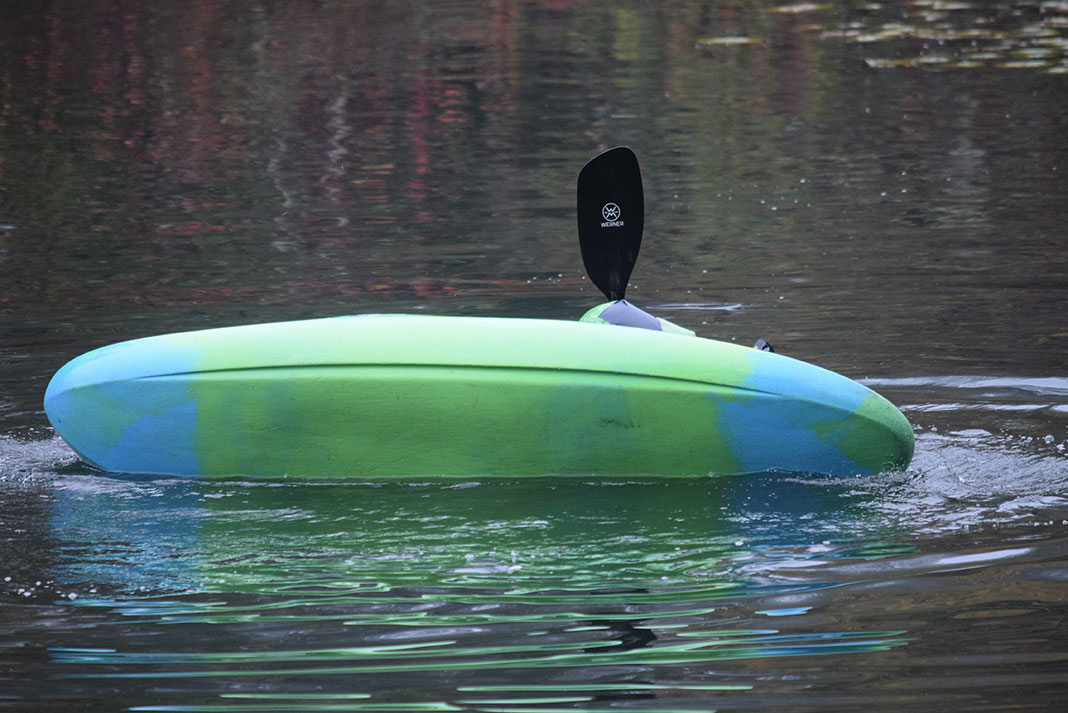 person rolls a whitewater kayak