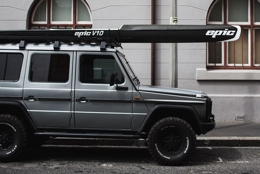 SUV parked on a city side street with an EPIC surf ski kayak on the roof rack