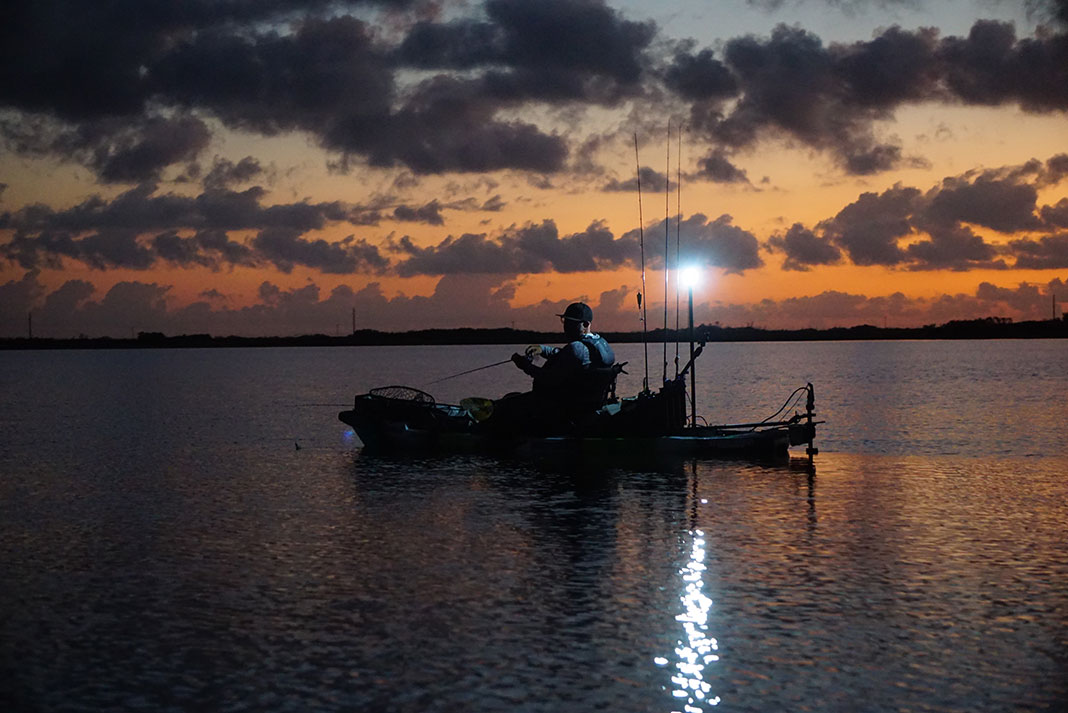 man fishes at dusk from a kayak equipped with the required safety lights