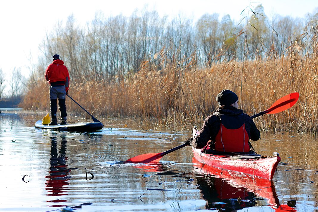 kayaker and paddleboarder paddle together in cold weather
