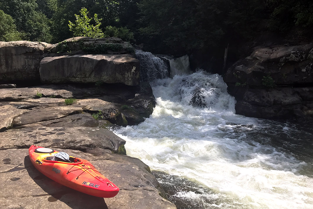 Whitewater kayak on rocks beside small set of falls on a river.
