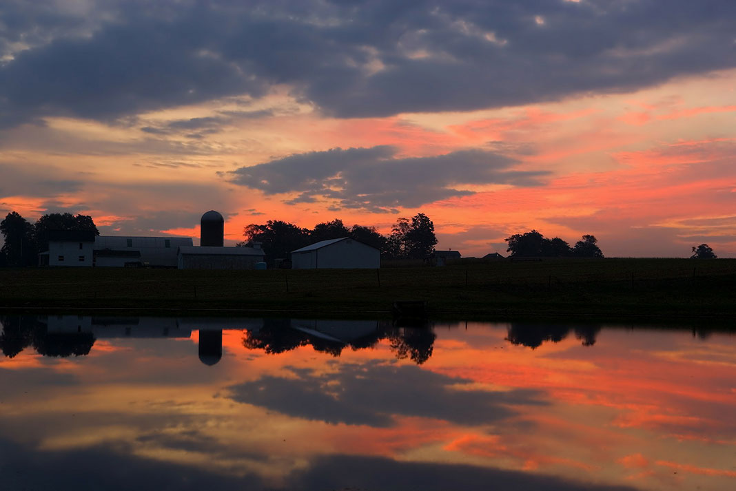 Ohio farm is silhouetted in the sunset and reflected in calm water