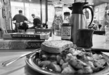 black and white photo of a lunch plate in a diner with a stack of paddling books and other people dining in the background