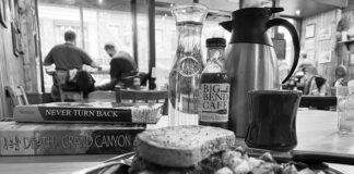 black and white photo of a lunch plate in a diner with a stack of paddling books and other people dining in the background