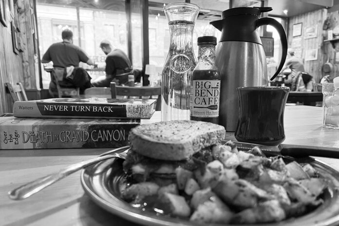 black and white photo of a lunch plate in a diner with a stack of paddling books and other people dining in the background