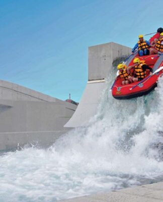 group of people in a river raft go over the artificial waterfall at Vector Wero Whitewater Park