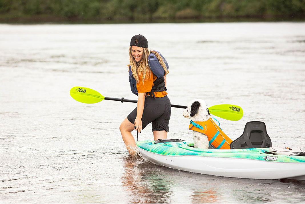 woman pulls Pelican Mustang 100x kayak with dog sitting in it