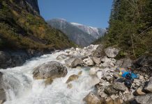 Person carrying whitewater kayak around river full of boulders