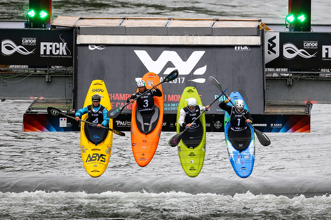 Four whitewater kayakers launching off a platform into the water.