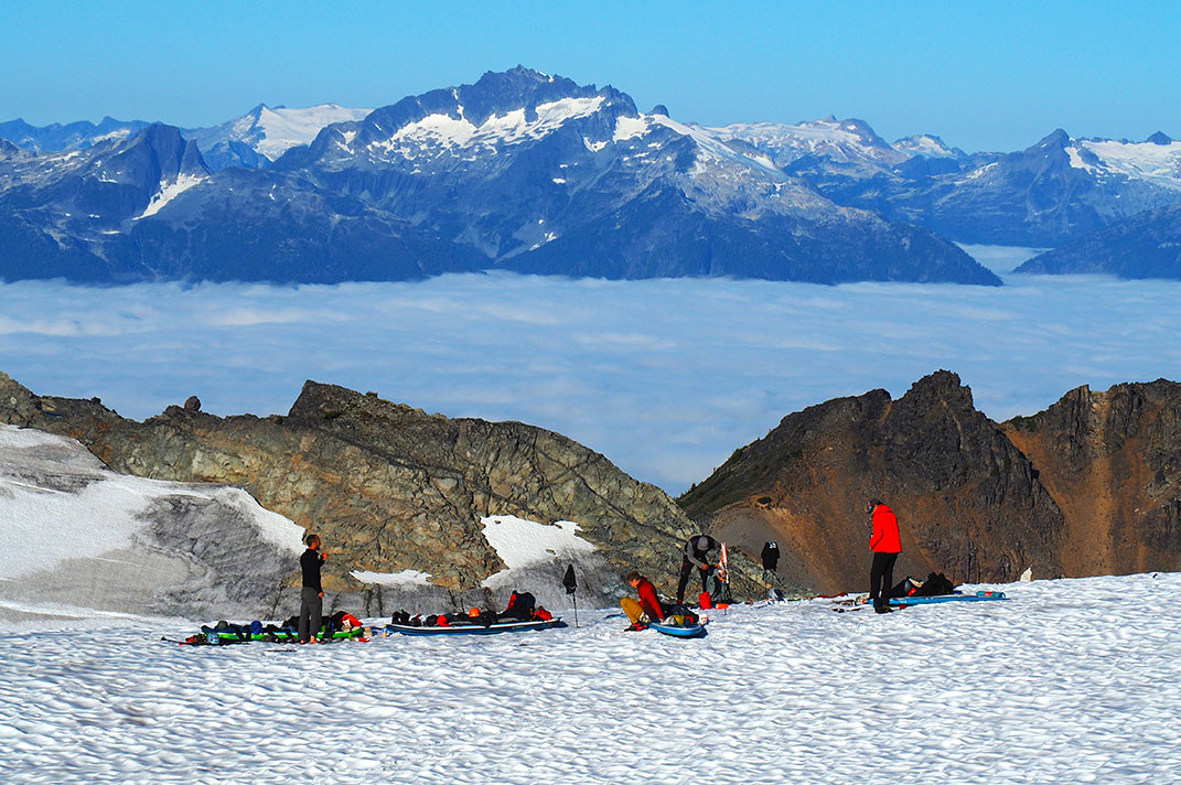 People setting up inflatable SUPs on snow at top of mountain.