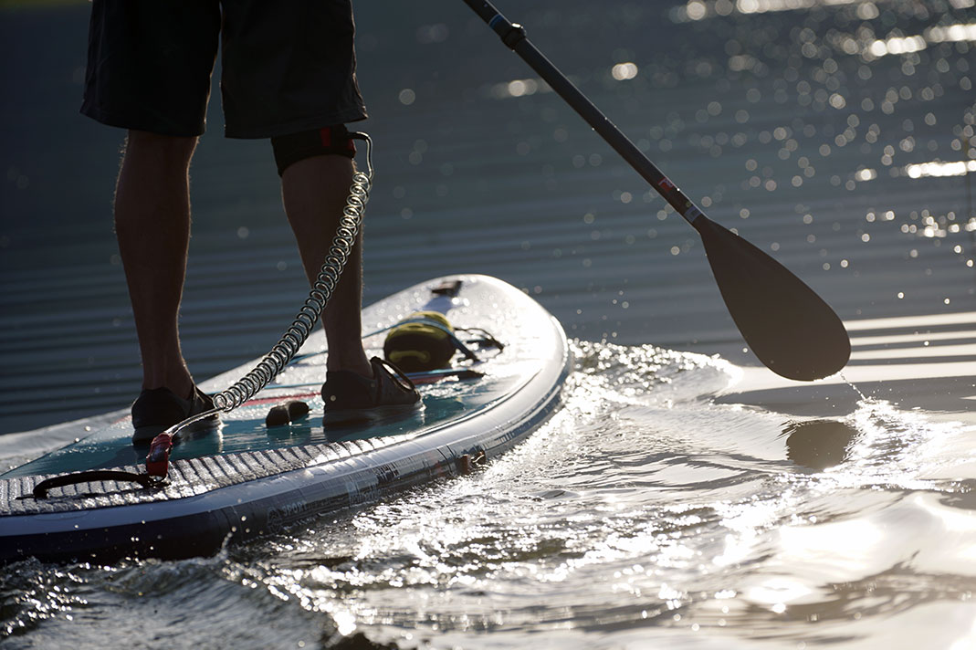 Man's feed on standup paddleboard with paddle posed to enter water.