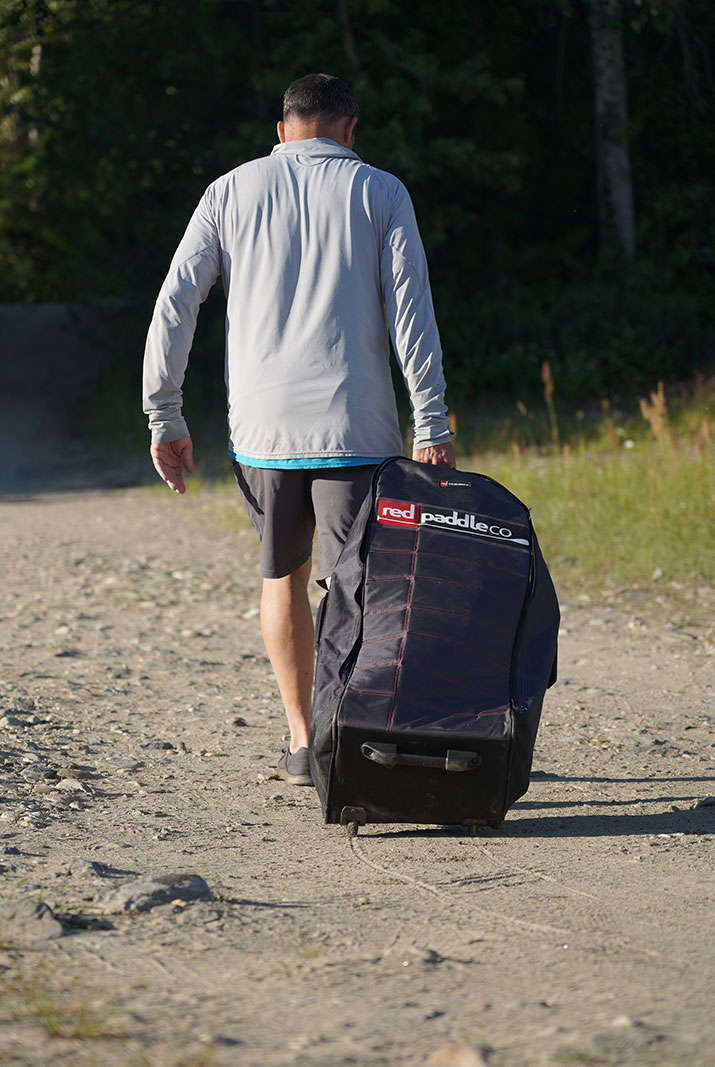 Man rolling black bag on dirt road.