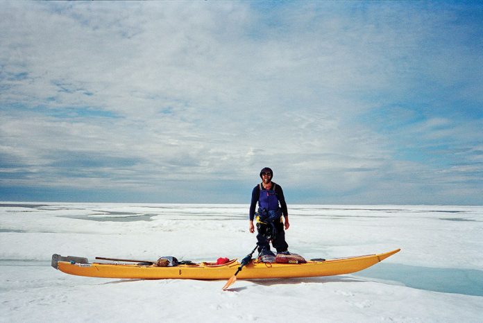 Man standing beside yellow sea kayak on snow.