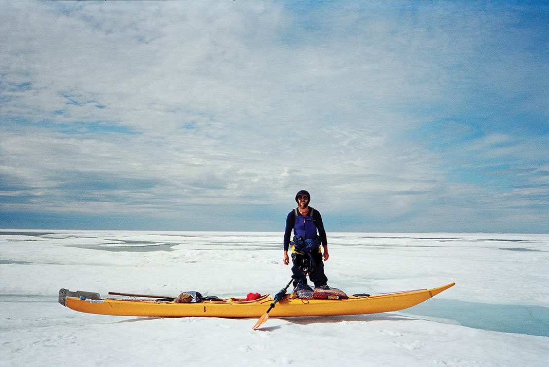 Man standing beside yellow sea kayak on snow.