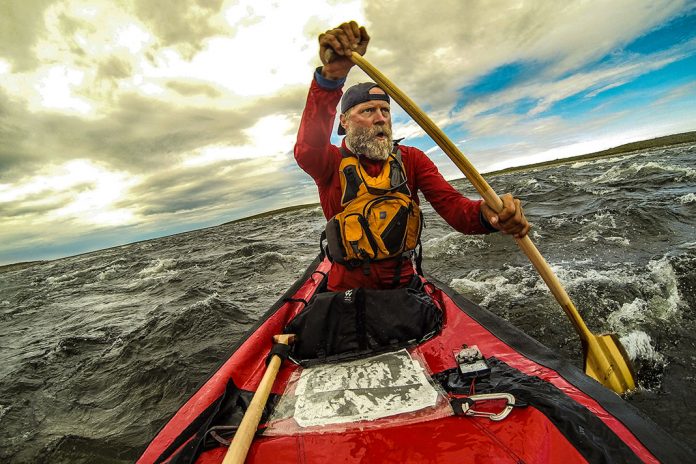 Man with beard paddling a canoe on choppy waters