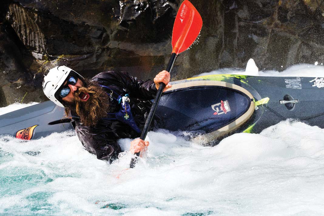 whitewater kayaker with beard opens his mouth as he leans hard through whitewater