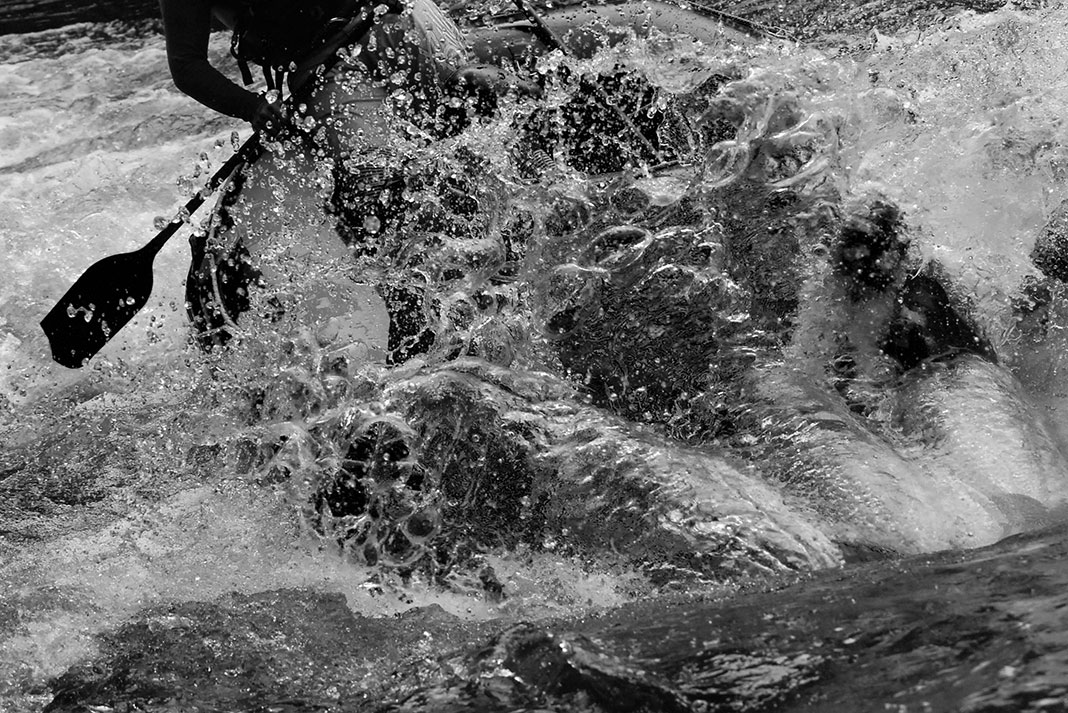 black and white photo of a person paddling a raft through whitewater