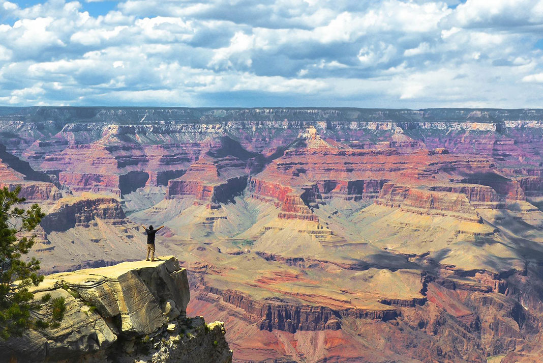 man stands with arms out at lookout over Grand Canyon