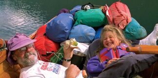 father and daughter laugh while eating lunch in a heavily loaded tripping canoe