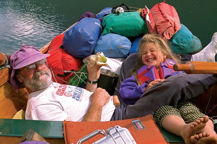 father and daughter laugh while eating lunch in a heavily loaded tripping canoe
