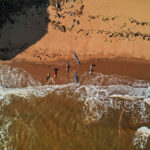 Learn How To Predict Tidal Currents For Sea Kayaking overhead photo of sea kayaks on a beach preparing to launch into surf