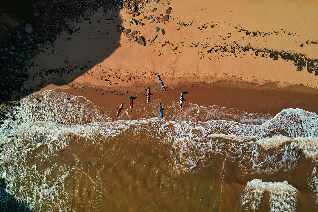overhead photo of sea kayaks on a beach preparing to launch into surf