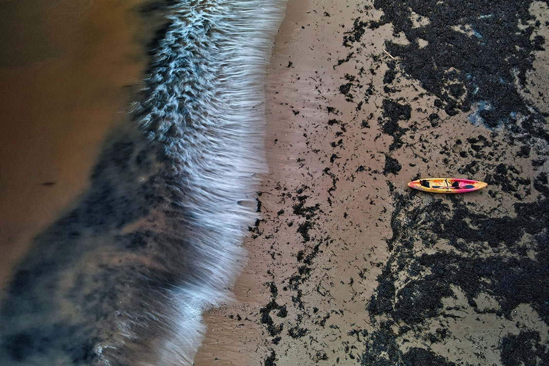 kayak sits on seaweed covered beach while waves crash to shore