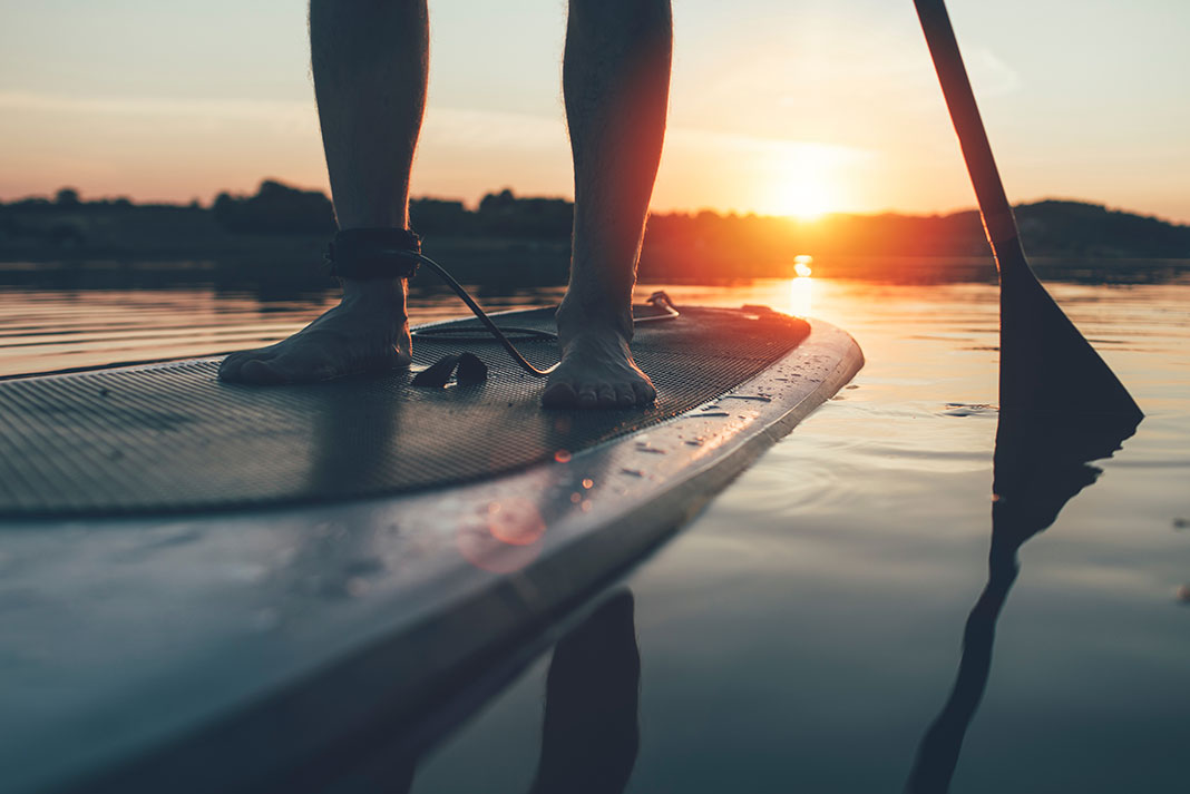 person standing and paddling on a SUP at sunset