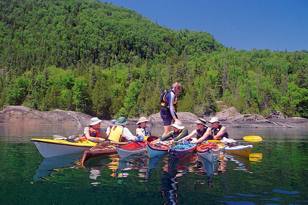 man stands up and walks across several kayaks with kayakers on the water