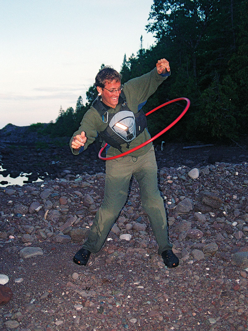 male kayaker hula hooping on the riverbank after a day of paddling