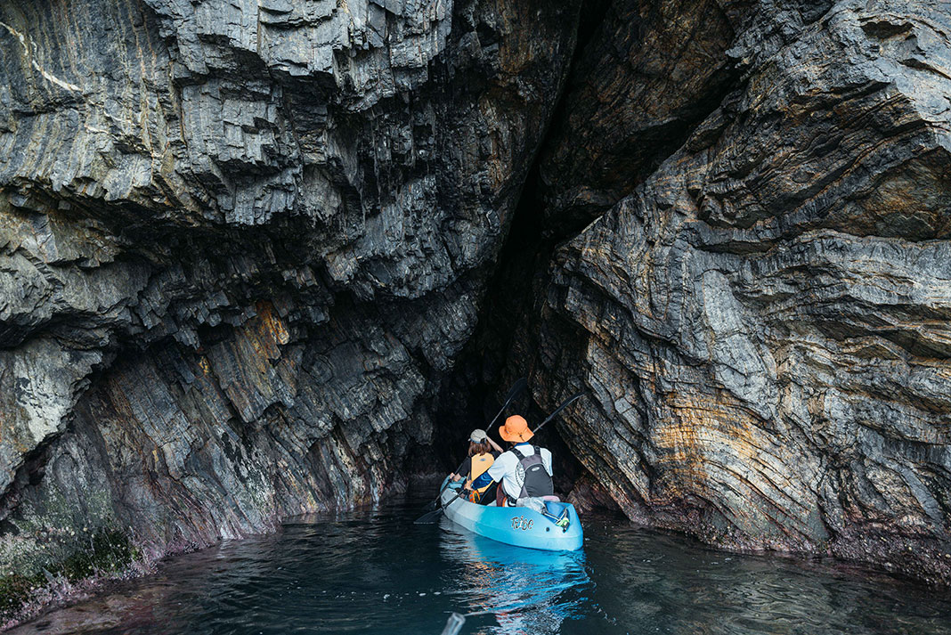 paddlers in a kayak explore oceanside caves